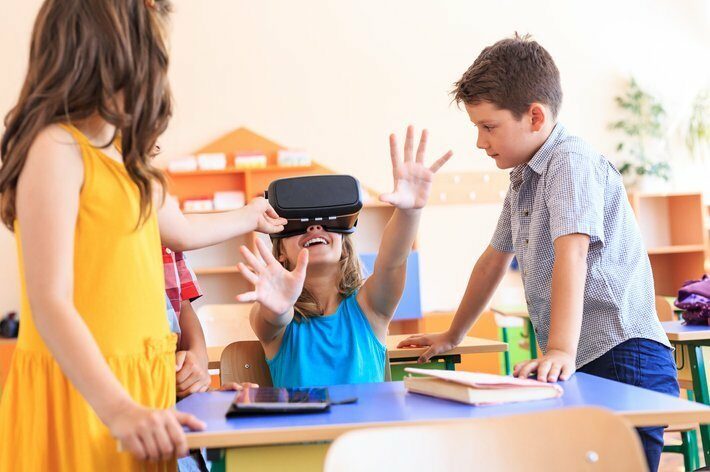 Students having fun in classroom, using VR headset.