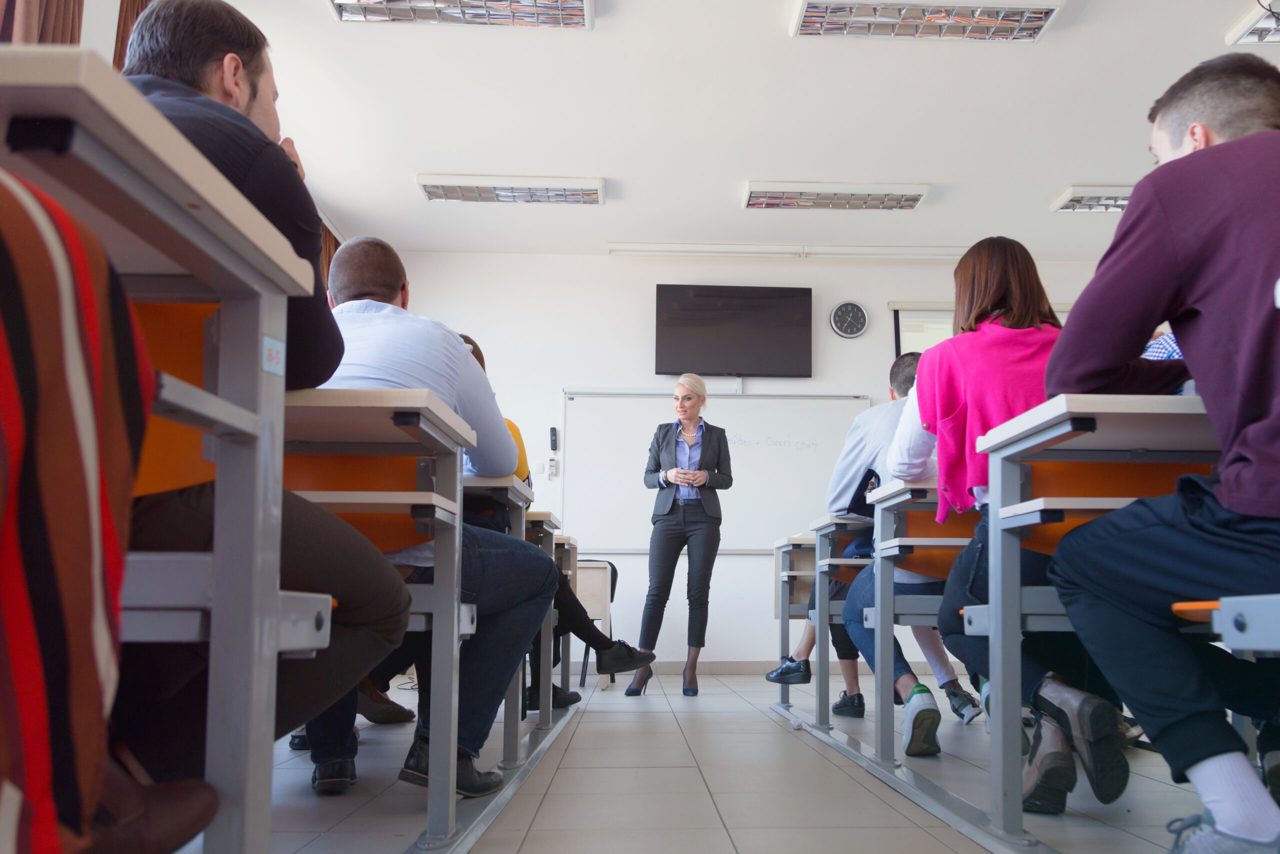 Female attractive professor explain lesson to students and interact with them in the classroom.Helping a students during class. University student being helped by female lecturer during class.